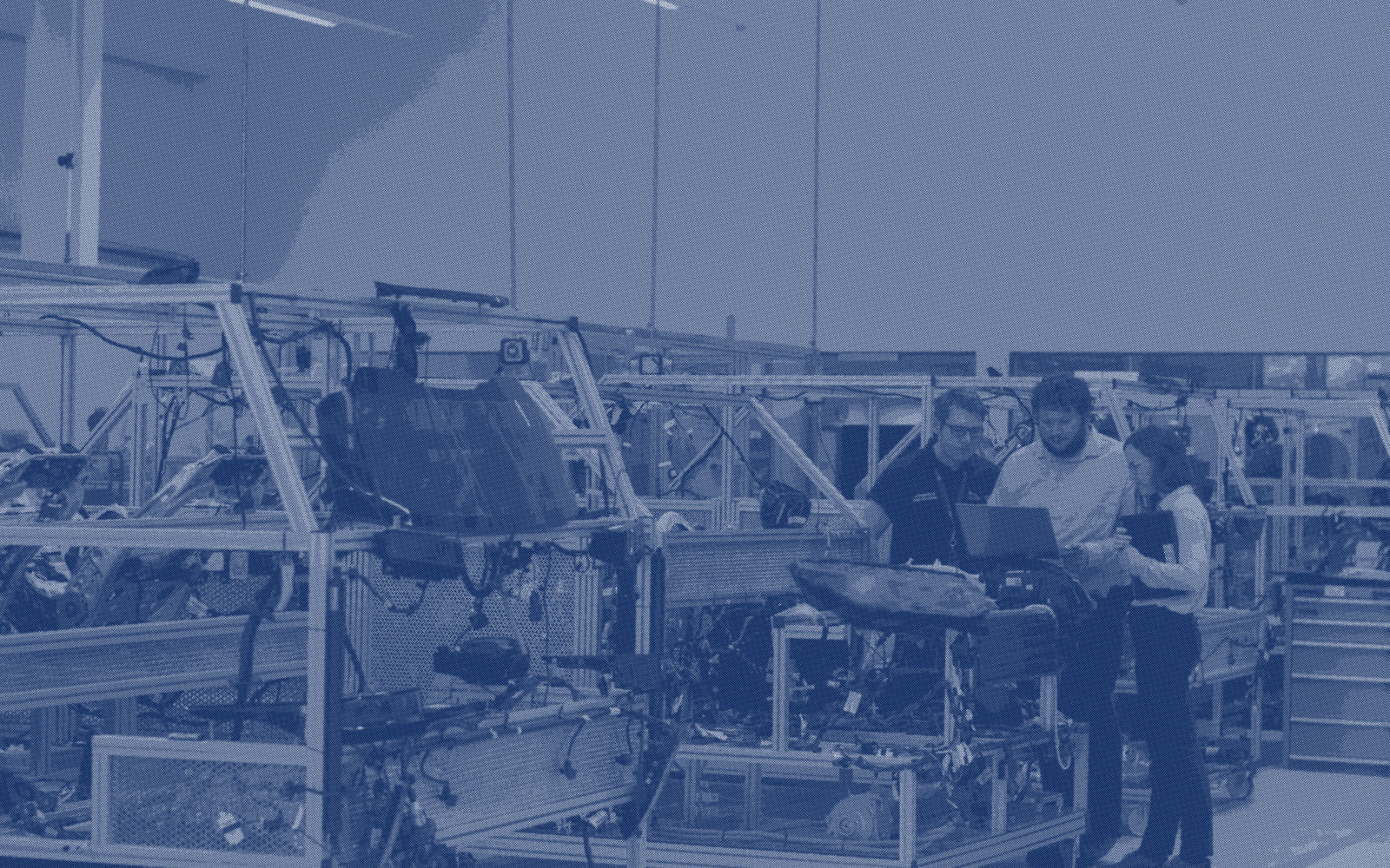 An assembly line in a production hall, with three people working at a bench beside the racks