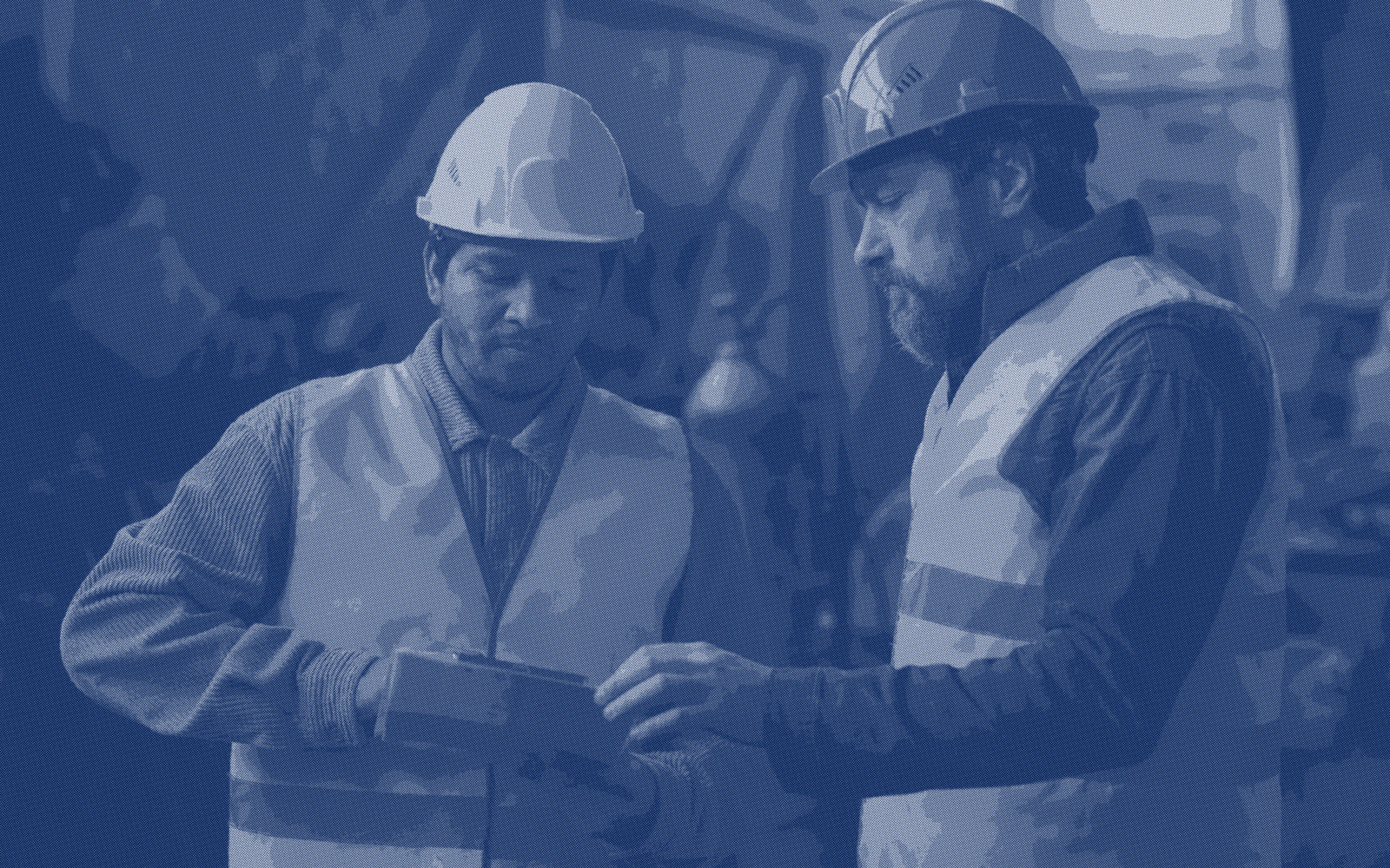 Two workers in hard hats and high-visibility vests standing side by side over a piece of equipment