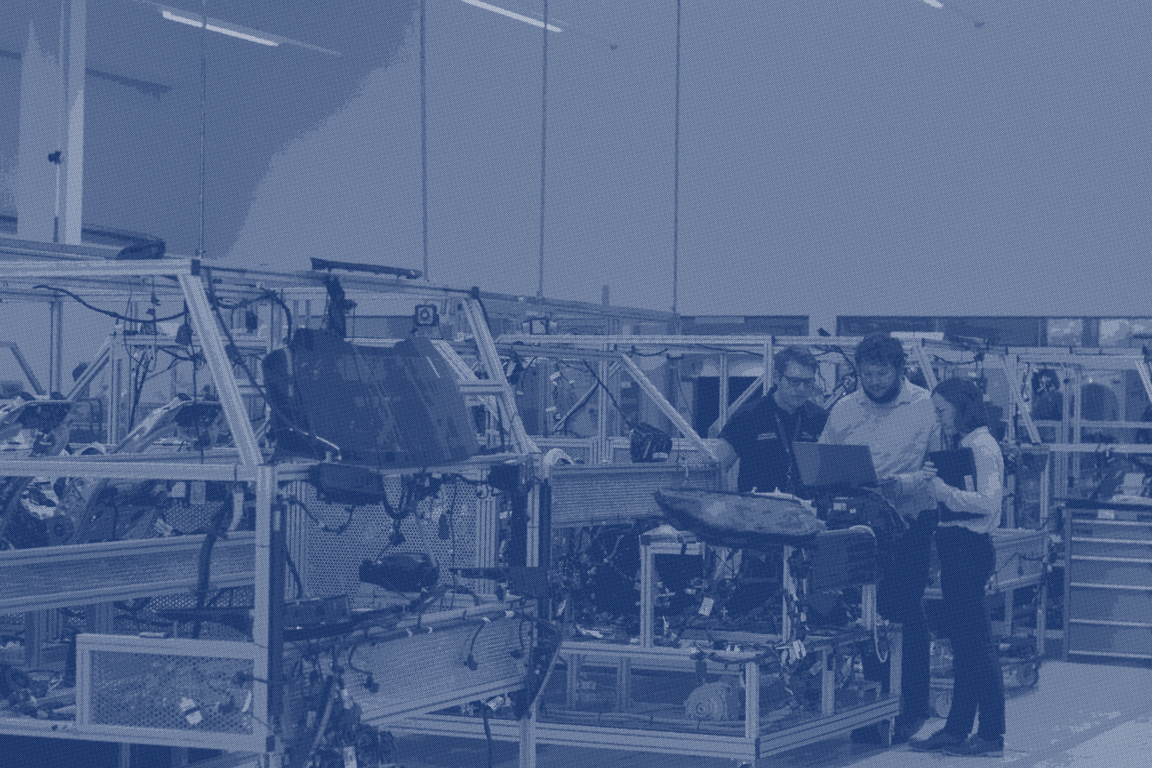 Three people standing together at the end of an assembly line, looking at a screen on a trolley