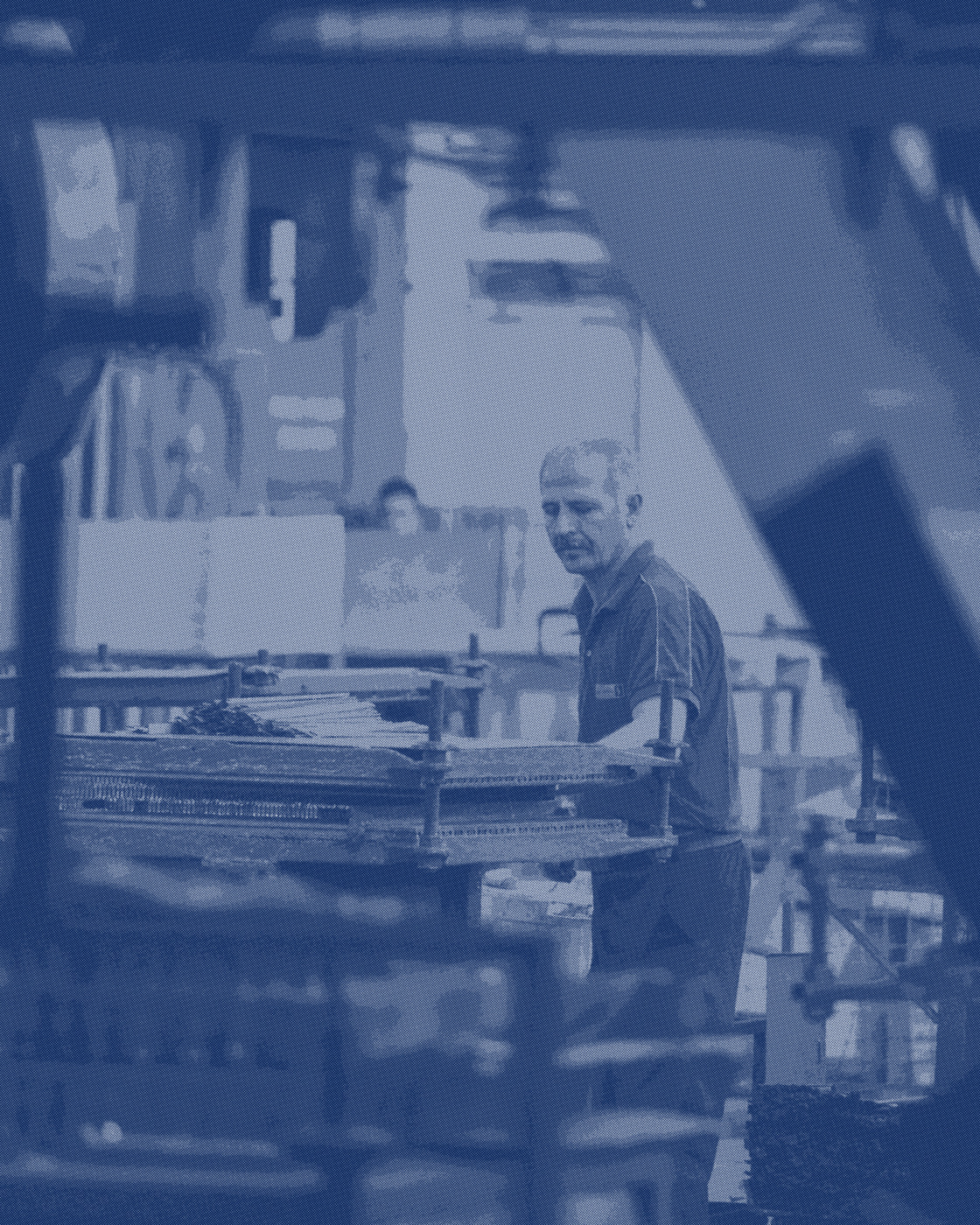 A worker alone at a bench in a plant, looking down at the piece in front of him