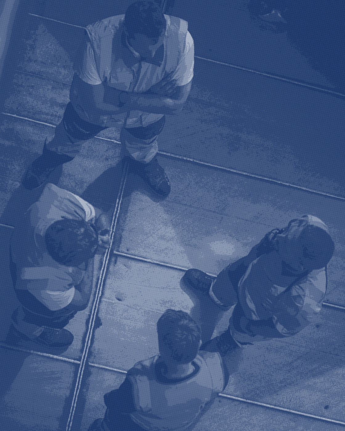 Four workers in high-visibility vests gathered on a marked concrete floor, seen from above