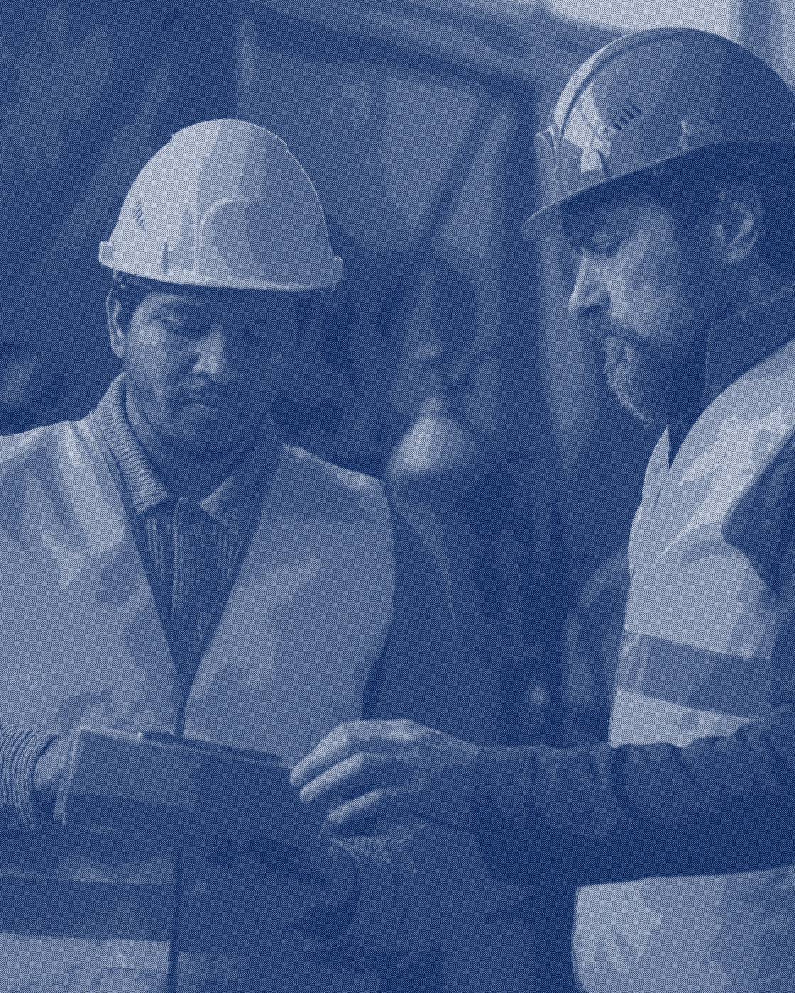 A supervisor and a worker looking through paperwork beside a workbench